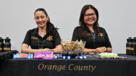Two Probation officers sit behind a table displaying Orange County Probation promotional items