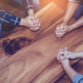 People sitting around a table with their hands together